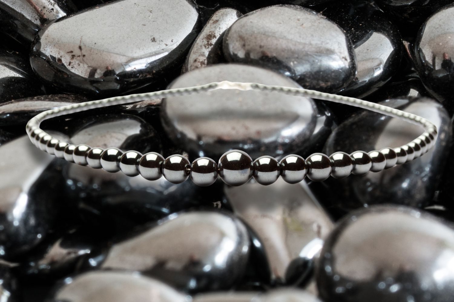 Hematit halsband med runda pärlor, placerat på glansiga tumlade hematit stenar.